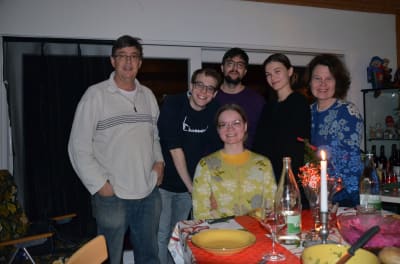 Familj på fem personer står och sitter vid ett bord.