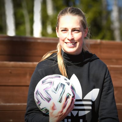 Linda Säälström sitter med bollen i handen i solskenet på läktaren vid planen i Korso 