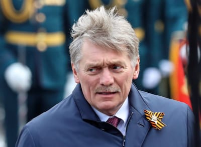  Viiksekäs Peskov on pukeutunut siniseen takkiin, kauluspaitaan ja viininpunaiseen kravattiin. Napinlävessä hänellä on Yrjönnauha, jota venäläiset pitävät voitonpäivänä.
