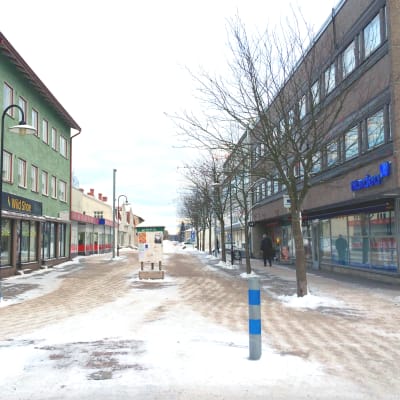 En folktom gågata. Till vänster och höger syns byggnader med olika affärer.