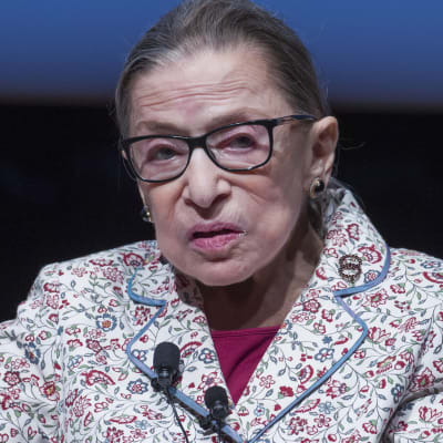 Ruth Bader Ginsburg sitter i en soffa med knappmikrofon på en blommig kavaj.