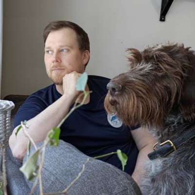Tauno Ljetoff katsoo ikkunasta sohvalla yhdessä koiransa Kuuran kanssa. 