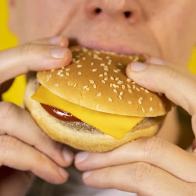 Lähikuva henkilöstä, joka syö hampurilaista