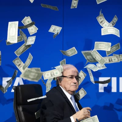 Kansainvälisen jalkapalloliiton puheenjohtaja Sepp Blatter istuu lehdistötilaisuudessa. Hänen ympärillään leijailee väärennöksiä Yhdysvaltain dollareista, jotka tilaisuuteen saapunut brittikoomikko heitti ilmaan kritisoidakseen Fifan korruptiota. Kuva on vuodelta 2015 Sveitsistä.