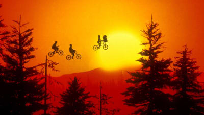 En rödtonad bild där man ovanom skogstopparna ser tre cyklister som flyger i luften.