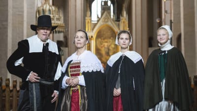 En man och tre kvinnor i gammaldags kläder står i Åbo domkyrka.