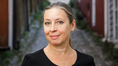 Medelålders kvinna poserar i en gränd med äldre trähus.