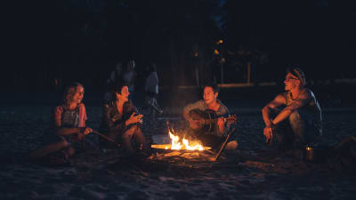 Fyra glada männsikor sitter och musicerar runt en lägereld i sommarnatten.