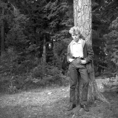 En ung Anders Wiklöf står lutad mot ett träd. 