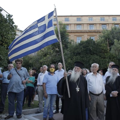 Grekisk-ortodoxa som håller i grekisk flagga demonstrerar i Aten.