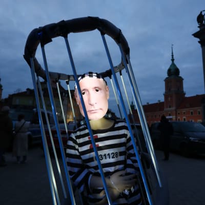 En docka i randiga fängelsekläder med ett Z på bröstet. Dockan är instängd i galler och har handbojor på. Dockans ansikte är täckt av en bild av Vladimir Putins ansikte.
