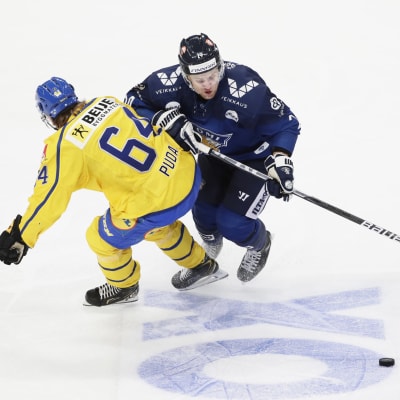 Finländsk spelare och svensk spelare i närkamp med pucken liggande på isen.
