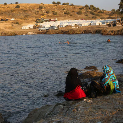 Kaksi turvapaikanhakija naista istuu meren rannalla Lesboksen saarella.