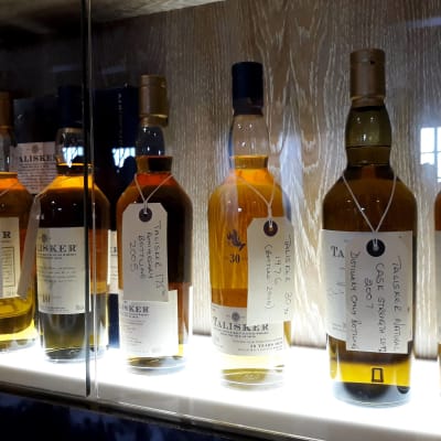 Whiskeyflaskor av märket Talisker uppradade på en upplyst hylla.