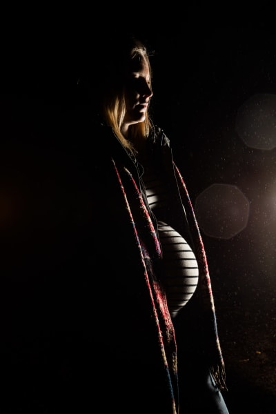 En gravid kvinna står på en grusväg i ett utomhusområde på natten. Kvinnans mörka profil tas från ficklampan som kommer bakom bilden. Den unga kvinnan kan inte identifieras på bilden.