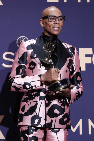 Närbild på RuPaul Charles i en ljusröd och svartblommig kostym med en Emmy-statyett i handen.