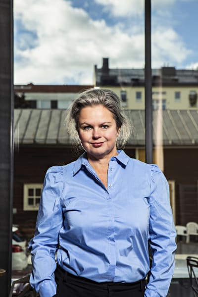 Teaterchef Ann-Luise Bertell i blå skjorta. I bakgrunden hus och blå himmel.