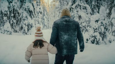 Far och dotter vandrar mot solen genom ett snötcäkt landskap.