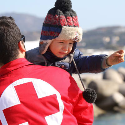 Röda Korset-medarbetare hjälper en flyktingpojke som anlänt till Kreta i Grekland.