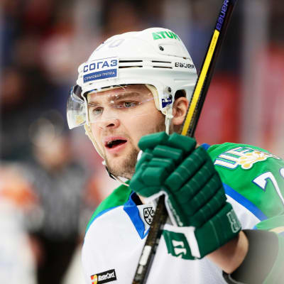 Grönklädd ishockeyspelare i profil följer med spelet från avbytarbänken.