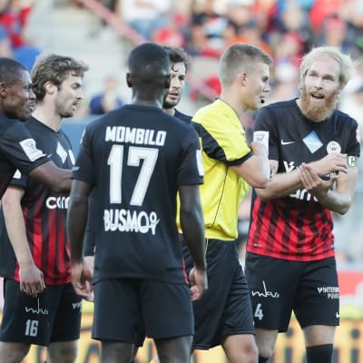 Svartklädda fotbollsspelare från PK-35 diskuterar vilt med domare.