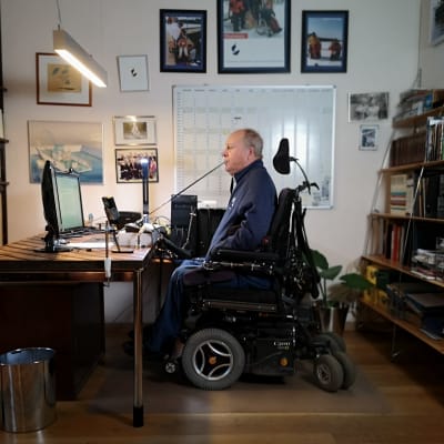 En man i elektrisk rullstol sitter framför en datorskärm i kontorsmiljö.