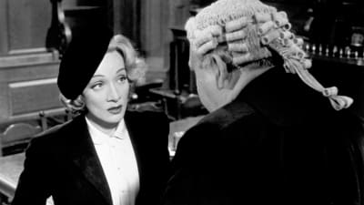 Baskeripäinen Christine Vole (Marlene Dietrich) peruukkipäisen asianajajan (Charles Laughton, selin) puhutettavana oikeussalissa. Kuva elokuvasta Todistaja (Witness for the Prosecution)