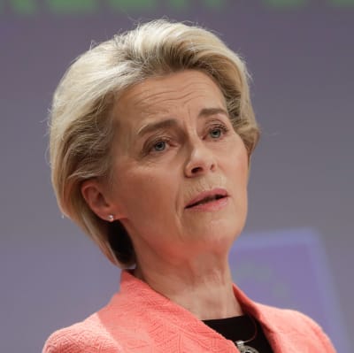 Ursula von der Leyen i rosa kavaj framför ett podium.