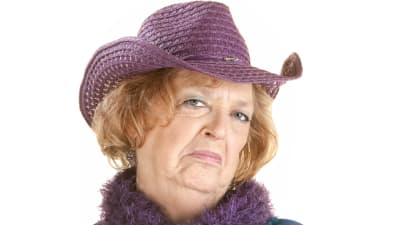 en äldre kvinna med hatt ser väldigt sur och bestämd ut medan hon tittar in i kameran. 