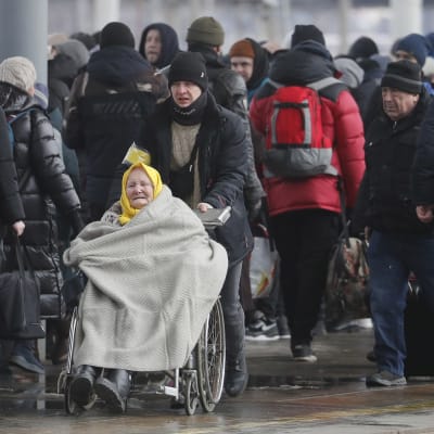 Vanha nainen rulatuolissa avustajansa kanssa ja muita pakenevia ukrainalaisia juna-aseman laiturilla.
