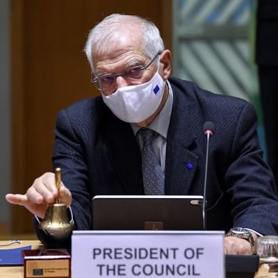 Maskikasvoinen Josep Borrell soitaa kelloa neuvottelupöydän ääressä