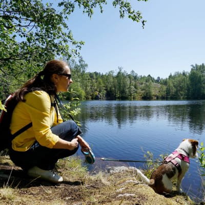 En kvinna sitter på huk med sin hund vid en sjö i skogen.