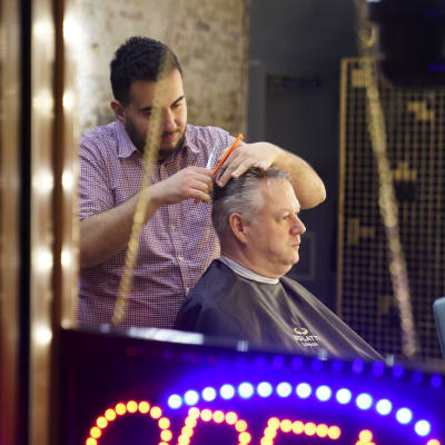 David Eburn sitter fotograferad genom fönstret till en frisörsalong där han får håret klippt.