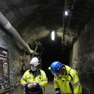 Ett hål i betonggolvet i en tunnel. Två män med stövlar och skyddsdräkter står bredvid