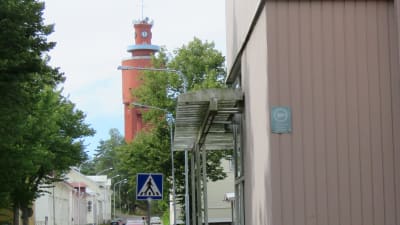 En gata (Skolgatan i Hangö) med några trähus och bilar parkerade längs gatan. I bakgrunden Hangös vattentorn.