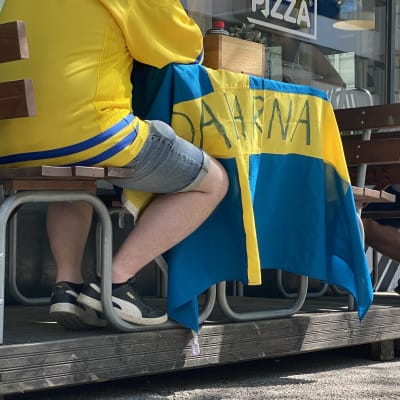 Ravintolan terassipöydälle on levitetty Ruotsin lippu. Pöydän ääressä istuu sinikeltaisiin vaatteisiin pukeutunut henkilö.
