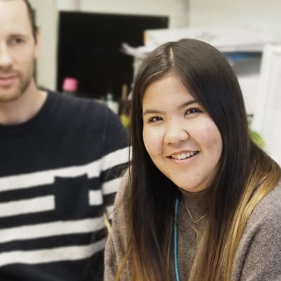 tyttö katsoo kameraa. Nainen ja mies taustalla katsovat tyttöä