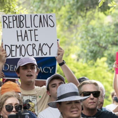 Lippalakkiin pukeutunut valkoinen mies mielenosoittaa. Kyltissä lukee englanniksi "republicans hate democracy".