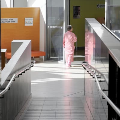 Sairaalan pyjamaan pukeutunut nainen kävelee sairaalan käytävällä.