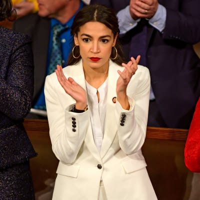 Alexandria Ocasio-Cortez i en vit kostym står och applåderar i USAs kongress.