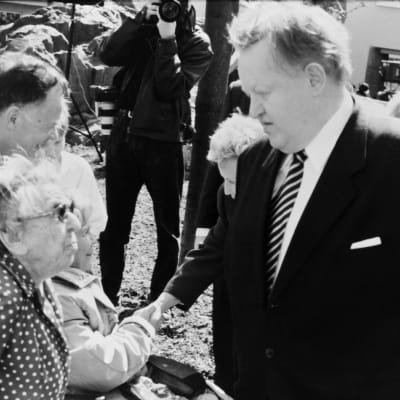 Martti Ahtisaari skakar hand med en kvinna på ett torg, omgiven av andra människor
