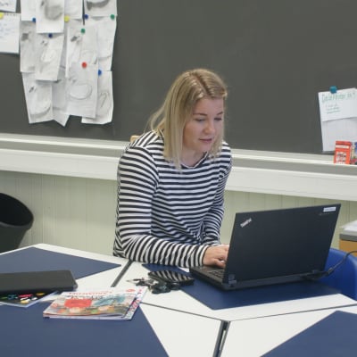 Jasmin Bilenberg sitter i ett tomt klassrum och undervisar eleverna med hjälp av dator. 