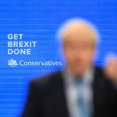 I bakgrunden testen: GET BREXIT DONE underskrivet av Conservatives. I förgrunden en helt suddig Boris Johnson som gestikulerar. 