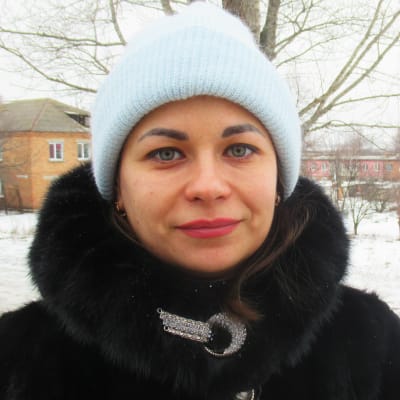 Anastasia Anizimova ser in i kameran med ett litet leende. Hon står i ett vintrigt landskap iklädd mössa och päls.
