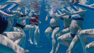 Gravida kvinnor syns gymnastisera under vattnet i en simbassäng.