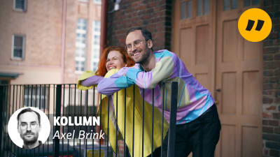 My och Axel befinner sig i en urban miljö, iklädda pastellfärgade kläder. My och Axel lutar mot ett metallräcke. De ser glada ut. Bakom dem syns en tegelvägg.