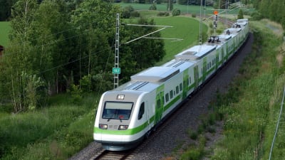 Ett passagerar tåg i vita och gröna färger kör fram i en svag kurva genom ett grönt och lummigt landskap. Järnvägen har bara ett spår.