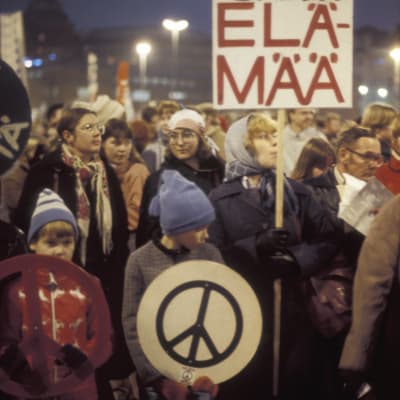 Mielenosoittajia, lapsia ja naisia kokoontuneena Helsingin Hakaniementorilla. Kyltti, jossa iskulause "Rauha ei tapa elämää" ja rauhanmerkki. Mielenosoitus rauhan puolesta.