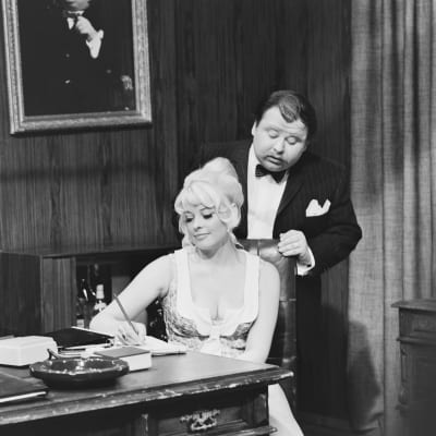 Kuva mustavalkoisesta tv-ohjelmasta "Akkavalta - Woman power" vuodelta 1969. Kuvassa johtajaa näyttelevä Jukka Sipilä ja sihteerinä Sirpa Fransman.