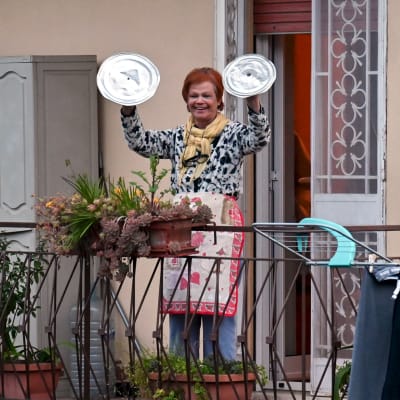 Kvinna deltar i tacksamhets- och glädjeyttring med kastrullock som cymbaler på en balkong i Rom 13.3. 2020 